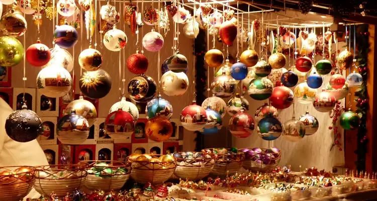 Primer plano de un puesto de mercado lleno de cientos de bolas y adornos de Navidad de cristal o cerámica, decoradas con motivos navideños y de paisajes nevados.